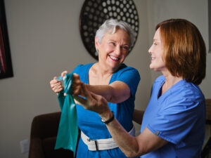 home health physical therapist helps older woman with an exercise involving a stretchy band